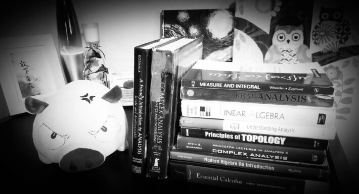 Picture of a bookshelf with books stacked up and an angry pig plushie beside it, in black and white